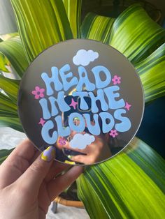 a hand holding up a mirror with the words head in the clouds on it and flowers