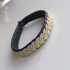 a close up of a black and gold bracelet on a white table with a wine glass in the background