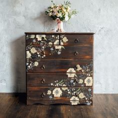 an old dresser with flowers painted on the front and drawers, sitting against a wall