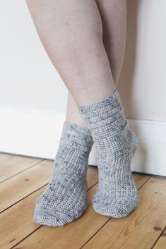 a woman's legs with socks on standing next to a wall and wooden floor