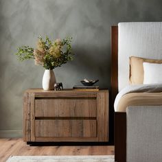 a bedroom with a bed, nightstand and flower vase on the end table in front of it