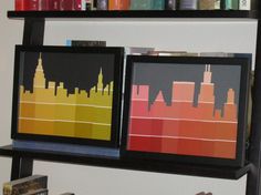 two framed cityscapes are sitting on a shelf in front of bookshelves