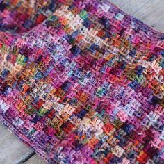 a multicolored crocheted blanket laying on top of a wooden table