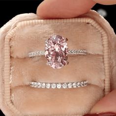 a pink diamond ring sitting on top of a velvet case in someone's hand