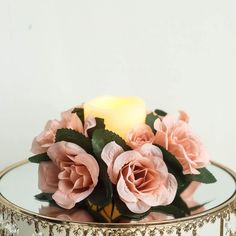 a candle that is sitting on top of a glass stand with flowers in it and leaves