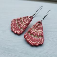 two pairs of red and gold earrings on top of a wooden table with white background