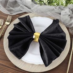 a black napkin with a gold ring on it sits on a white plate next to silverware