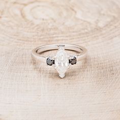 a white diamond ring with black stones on it sitting on a piece of tree bark