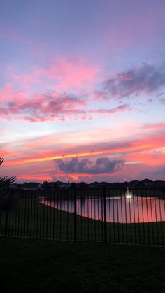 the sun is setting over a lake and fence