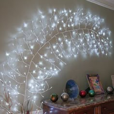 a decorative tree with white lights on it's branches in front of a wall