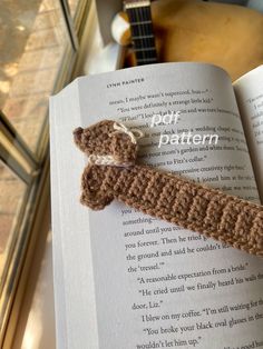 a crocheted bookmark laying on top of an open book next to a guitar