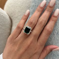 a woman's hand wearing a ring with an emerald stone