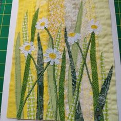 a piece of fabric with daisies and green grass in the background on a cutting board