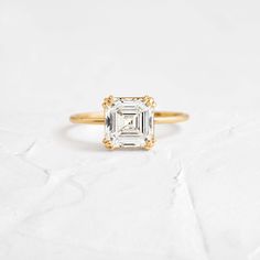 a gold ring with an emerald cut diamond in the center, on a white background