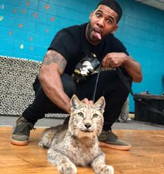 a man sitting on the floor with a cat in front of him and his tongue hanging out