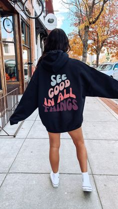 "This oversized hoodie is the perfect way to stay cozy and comfy while looking stylish. The unisex design features a hood, long sleeves, and a kangaroo pocket. The back proudly displays the words \"See Good In All Things\" in a bold retro wavy font to remind the person behind you of the good in life. The hoodie is made from super soft fabric for extra comfort, and the relaxed fit ensures you'll look great no matter how you wear it. Gildan 18500 50% cotton, 50% polyester Medium-heavy fabric  Classic fit Tear-away label Runs true to size Let me know if you have any questions! Xo, Bobbi" Positive Message Hoodie, Hoodies With Quotes On Back, Printed Hoodies Ideas, Hoodie Design Ideas Aesthetic, Trendy Hoodie Designs, Quotes Hoodies, See Good In All Things, Wavy Font, Motivational Hoodies