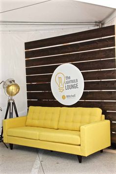 a yellow couch sitting in front of a wall with a light bulb sign on it