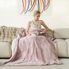 a woman sitting on a couch with a pink blanket