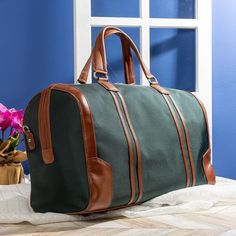 a green duffel bag sitting on top of a bed next to a vase with flowers