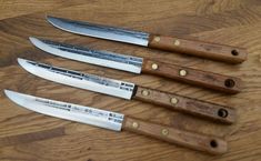 four knives are sitting on a wooden table