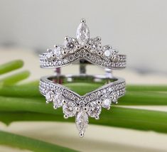 two wedding rings sitting on top of each other next to green stems and flowers with leaves in the background