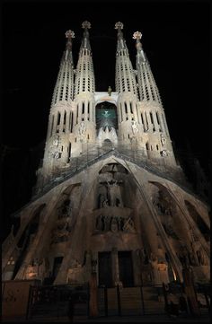 the cathedral is lit up at night with lights on it's spires and statues