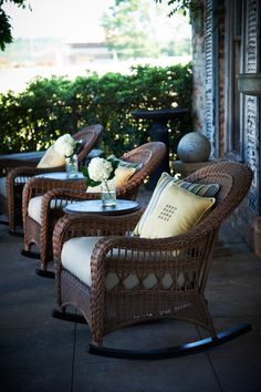 wicker chairs and tables on a patio with flowers in vases next to them