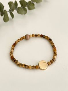 the bracelet has a gold disc on it and is surrounded by brown beads with green leaves