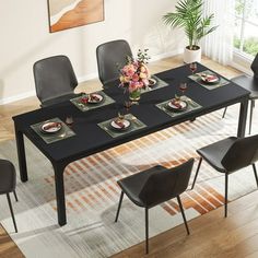 a dining room table set with black chairs and plates on the placemat in front of it