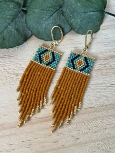 two pairs of beaded earrings sitting on top of a wooden table next to a leaf