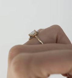 a woman's hand holding up a gold ring with a diamond on the side