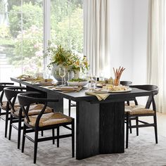 a dining room table set for six with chairs and place settings on the table in front of large windows