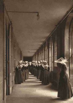 an old black and white photo of women in long dresses lined up at the end of a hallway