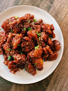 a white plate topped with meat covered in sauce and green onions on top of a wooden table