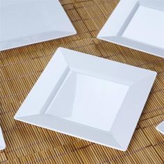 four white square plates sitting on top of a bamboo tablecloth covered placemats