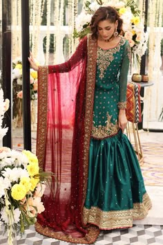 a woman in a green and red lehenga standing next to a flower arrangement