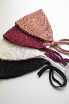 four knitted hats are lined up on a white surface, one has a knot at the top