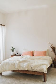 a bed with two pillows on it in a room next to a window and potted plants