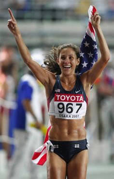 a woman holding an american flag in her hand and smiling at the camera as she crosses the finish line