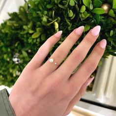 a woman's hand with pink manicured nails and a pearl ring