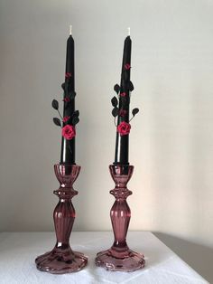 two pink glass candlesticks with roses on them sitting on a white table cloth