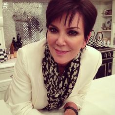 a woman sitting at a table in a kitchen wearing a white jacket and black scarf