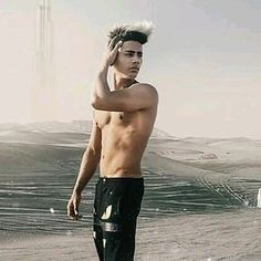 a shirtless man standing in the desert with his hand on his head while looking off into the distance