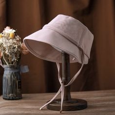 a pink hat sitting on top of a wooden table next to a vase with flowers