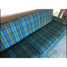 a blue and green plaid couch sitting on top of a carpeted floor next to a wall