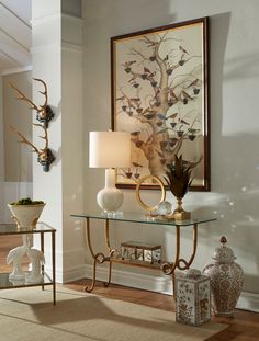 a glass table topped with two vases next to a lamp and painting on the wall