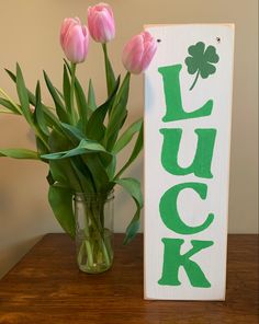 pink tulips are in a vase next to a sign that says luck