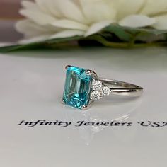 Paraiba Tourmaline Ring, Emerald Cut Engagement Ring 14K Gold, Three Stone Ring, Paraiba Ring For Ladies, Art Deco Paraiba Ring, #6311 This ring is an emerald cut lab created neon blue paraiba with round moissanite sides, 14k white gold # 6311 We feature the finest quality of lab grown stones in the world. The properties of lab-grown are physically, chemically and visually identical to natural, just grown in a lab setting. -Approximate total carat weight: 3.85ctw. diamond equivalent -Center Ston Gia Certified Tourmaline Rings For Formal Occasions, Gia Certified Trillion Cut Diamond Ring As Gift, Gia Certified Radiant Cut Sapphire Ring Gift, Fine Jewelry Tourmaline Rings With Brilliant Cut, Gia Certified Tourmaline Jewelry For Anniversary, Anniversary Tourmaline Jewelry In Baguette Cut, Baguette Cut Tourmaline Jewelry For Anniversary, Anniversary Baguette Cut Tourmaline Jewelry, Tourmaline Ring With Prong Setting For Anniversary