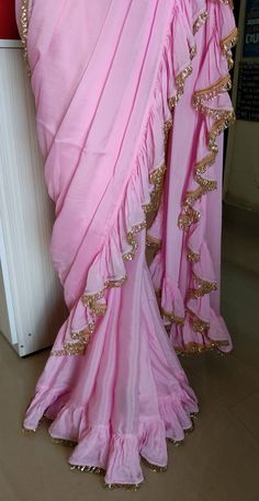 Color : Pink Fabric - Chinon This Ruffled Saree has beautiful Crystal Scallop trim at the hemline. Length of Saree 48 inches. Blouse : Pink Emroidered Net with Silk Lining The blouse and underskirt/petticoat will be stitched as per the measurements provided IF YOU WISH TO PURCHASE THIS WE CAN SEND A VIDEO ON YOUR WHATSAPP NUMBER FOR BETTER UNDERSTANDING OF THE SAREE Fabric Care : Dry Clean Only Disclaimer: The actual color of the product might slightly differ from the image due to photographic l Floor-length Ruffled Saree For Reception, Semi-stitched Sharara With Ruffles And Traditional Drape, Bollywood Style Sharara With Ruffles And Traditional Drape, Traditional Wear With Ruffles And Traditional Drape, Festive Floor-length Blouse Piece With Ruffles, Festive Floor-length Blouse With Ruffles, Bollywood Style Silk Blouse Piece With Ruffles, Navratri Ruffled Sharara With Traditional Drape, Traditional Sharara With Ruffles For Navratri