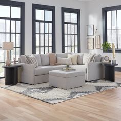 a living room filled with furniture and lots of windows in the wall behind it is a large rug on top of a hard wood floor